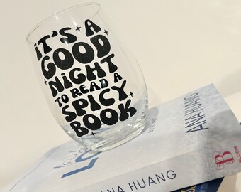 Könnte beinhalten: Ein klares Weinglas aus Glas mit einem schwarzen Vinyl-Aufkleber, auf dem "It's a good night to read a spicy book" steht. Das Glas steht auf zwei Büchern. Das obere Buch ist weiß mit blauem Text, auf dem "Twisted Love" und "Ana Huang" steht. Das untere Buch ist blau mit weißem Text, auf dem "It Happened One Summer" und "Tessa Bailey" steht.