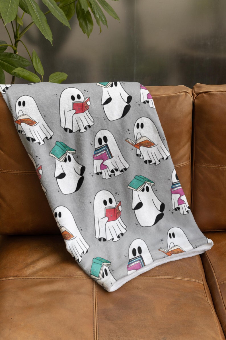 May include: A gray fleece blanket with a repeating pattern of white ghosts reading books. The ghosts are holding books of various colors and sizes.