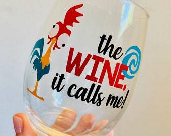 Puede incluir: Una copa de vino de vidrio transparente con un diseño de gallo rojo, azul y amarillo y el texto "the WINE, it calls me!"