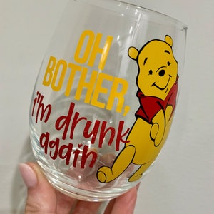 Könnte beinhalten: Ein klares Weinglas aus Glas mit einem gelben und roten Winnie Puuh-Design. Das Glas trägt den Text "Oh bother, I'm drunk again".
