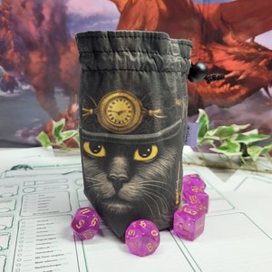 Könnte beinhalten: Ein schwarzer Würfelbeutel mit einem Katzen- und Uhr-Design. Der Beutel hat einen Kordelzugverschluss und ist von lila Würfeln umgeben. Der Hintergrund zeigt eine Fantasy-Illustration. Der Beutel ist etwa 15 cm hoch.