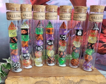 Può includere: Otto provette di vetro riempite con dadi colorati, ogni provetta ha un'etichetta che dice "HALLOWEEN". I dadi sono di vari colori, tra cui verde, arancione, nero e viola.