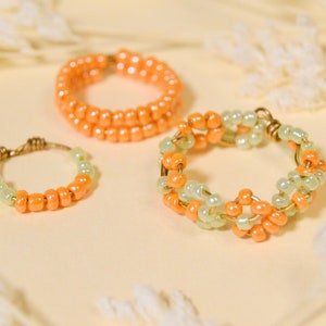 Op de afbeelding: Drie kralenringen in perzik en lichtgroen. De ringen zijn gemaakt van kleine kralen die aan draad zijn geregen.