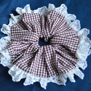 Könnte beinhalten: Ein Haargummi aus braunem und weißem Gingham-Stoff mit weißer Spitzenborte.