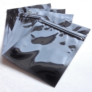 Op de afbeelding: Een stapel van vijf zwarte plastic zakken met ritssluiting en een heldere, glanzende afwerking.