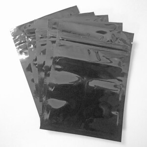 Pu&ograve; includere: Un mucchio di sacchetti di plastica neri, lucidi e con cerniera. I sacchetti sono disposti piatti su una superficie bianca.