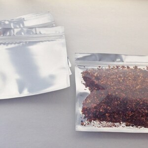 May include: Two silver zippered pouches, one empty and one filled with red and brown dried chili flakes.