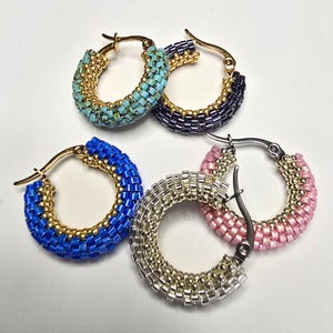 May include: Four hoop earrings featuring intricate beadwork in turquoise, dark purple, bright blue, silver, and light pink. Each earring is constructed with metallic gold or silver-toned metal hoops and small, uniform glass beads arranged in a textured pattern.