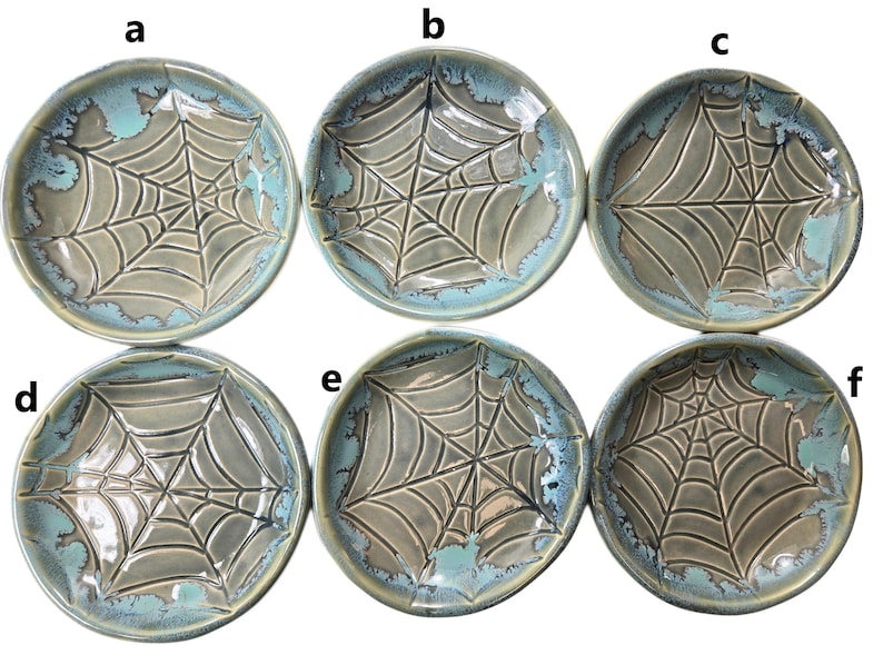 May include: Six ceramic plates with a spiderweb design. The plates are round with a gray center and a turquoise blue rim. The spiderweb design is raised and textured, adding depth to the plates. These plates are ideal for Halloween or spooky-themed decor.