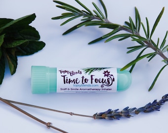 May include: A light green aromatherapy inhaler with the text "Time to Focus" and "Sniff & Smile Aromatherapy Inhaler". The inhaler is surrounded by sprigs of rosemary, mint, and lavender on a white background.