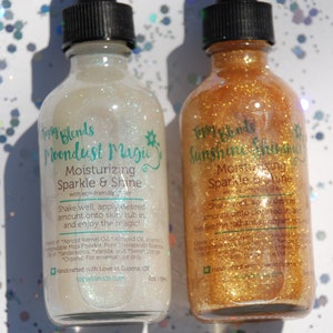 May include: Two glass bottles with gold and white glitter inside. The bottles are labeled "Topsy Blends Moondust Magic Moisturizing Sparkle & Shine" and "Topsy Blends Sunshine Shimmer Moisturizing Sparkle & Shine".