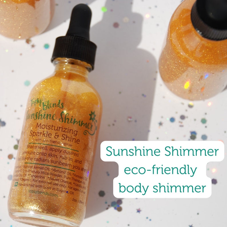 May include: A glass bottle with a gold shimmer body lotion. The bottle has a black dropper top and a white label with the text "Sunshine Shimmer Moisturizing Sparkle & Shine with eco-friendly glitter". The bottle is sitting on a white surface with gold glitter.