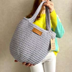 May include: A light purple crocheted tote bag with leather handles and a brown leather tag that says "Crocheted by Lunar Cat".