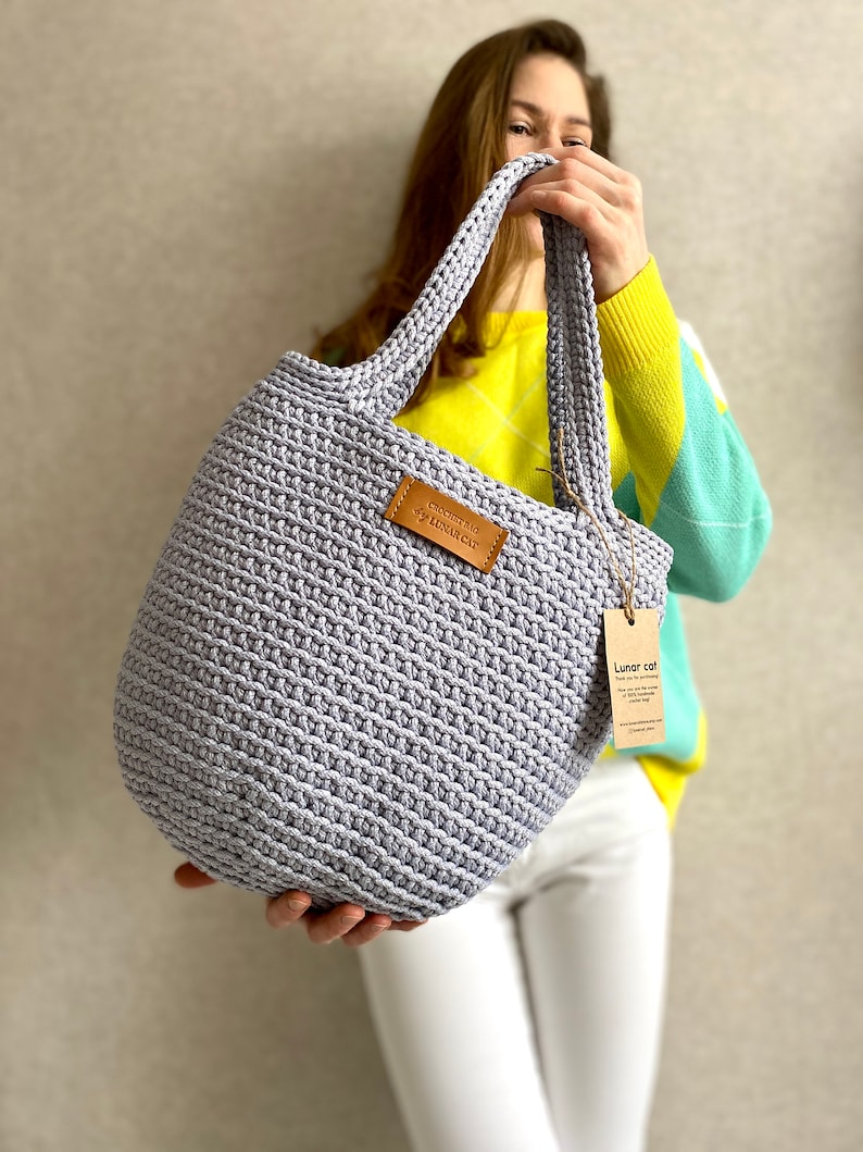 May include: A light purple crocheted tote bag with leather handles and a brown leather tag that says "Crocheted by Lunar Cat".