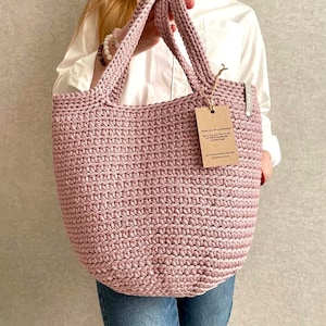 May include: A pink crocheted tote bag with a brown tag that says "Thank you for purchasing..." The tag also includes the website address "www.handmadewithlove.com".
