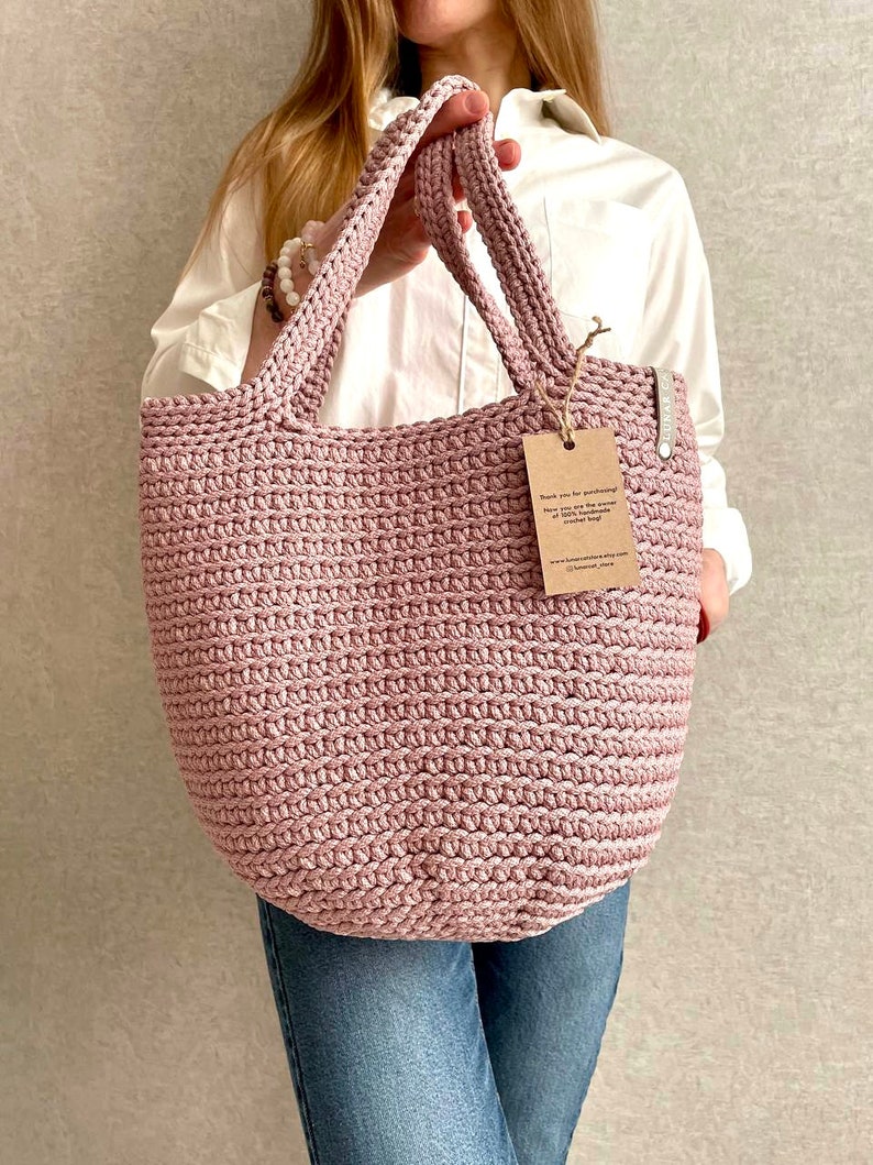 May include: A pink crocheted tote bag with a brown tag that says "Thank you for purchasing..." The tag also includes the website address "www.handmadewithlove.com".