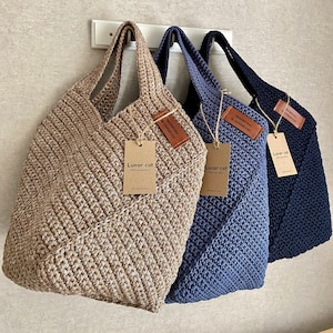 May include: Three crocheted tote bags in different colors and patterns. The bags are made of natural fibers and have a simple, elegant design. The bags are labeled with the text "Lunar Cat" and "Crochet Bag".