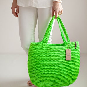 May include: A bright green crocheted tote bag with brown leather handles. The bag is made of thick yarn and has a simple, classic design.