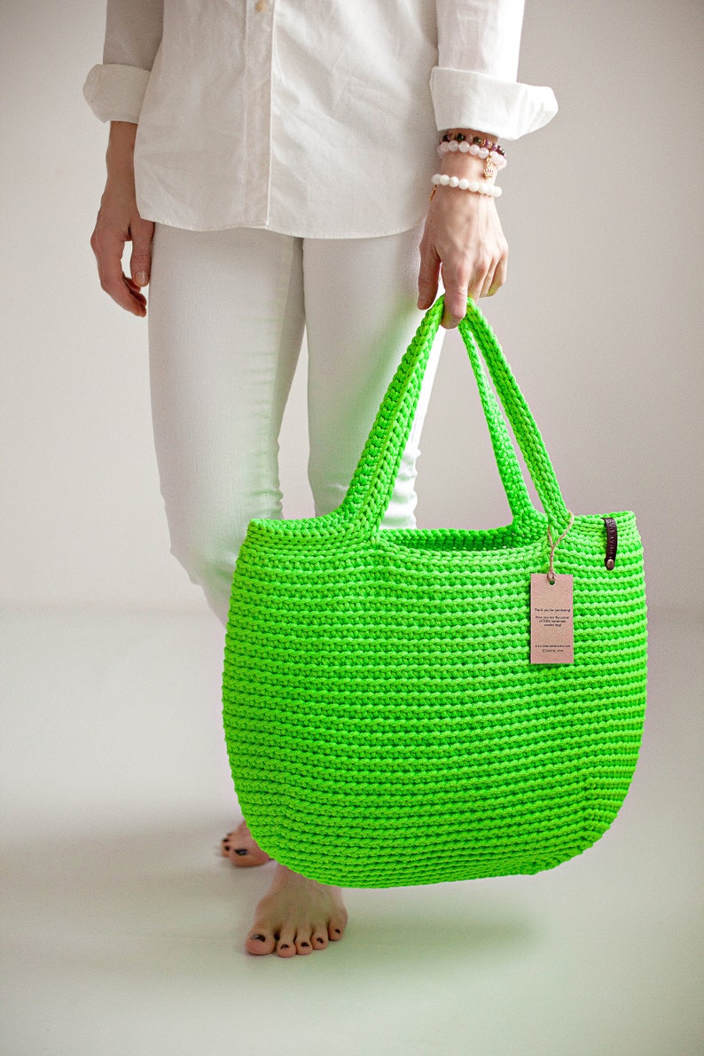 May include: A bright green crocheted tote bag with brown leather handles. The bag is made of thick yarn and has a simple, classic design.