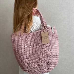 May include: A pink crocheted tote bag with a brown paper tag that says "Thank you for purchasing this handmade crochet market bag".