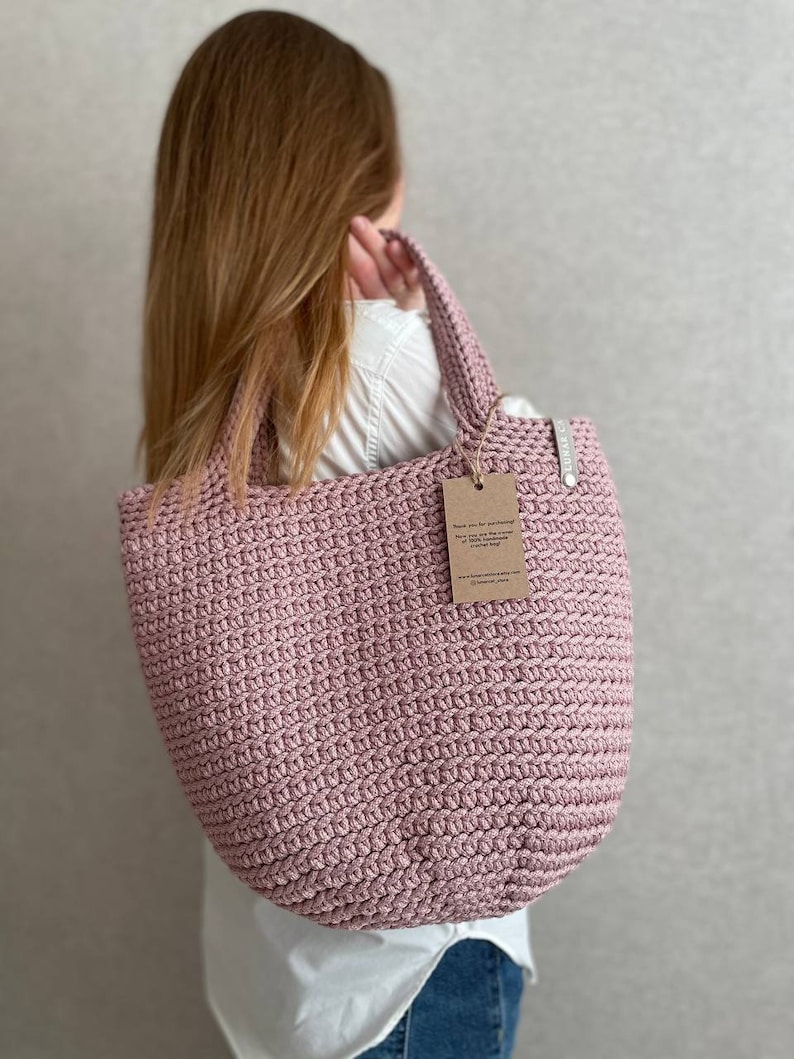 May include: A pink crocheted tote bag with a brown paper tag that says "Thank you for purchasing this handmade crochet market bag".