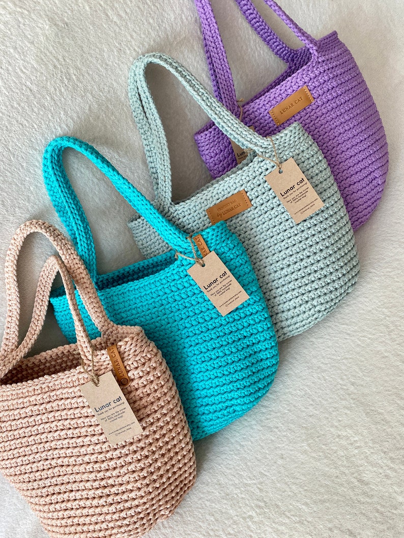 May include: Four crocheted tote bags in different colors: beige, turquoise, light green, and lavender. Each bag has a leather tag with the text "Lunar cat" on it.