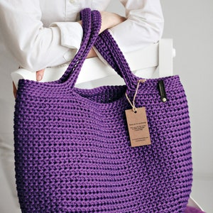 May include: A large purple crocheted tote bag with thick straps. The bag is made of a soft, textured yarn and has a simple, classic design.