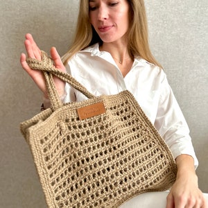 May include: A beige crocheted tote bag with a leather label that says "Crochet by Alejandra".