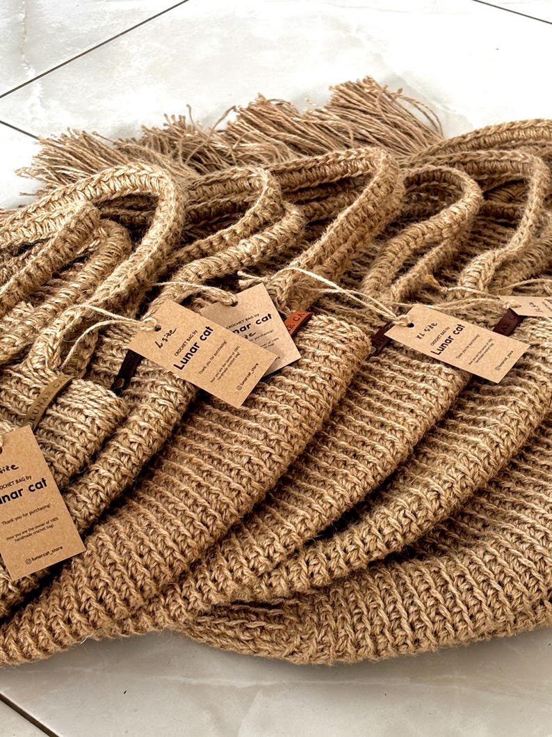 Puede incluir: Una pila de varias bolsas de crochet de yute marr&oacute;n con asas. Cada bolsa tiene una etiqueta que dice "Lunar Cat". Las bolsas est&aacute;n hechas de un material grueso y tejido y tienen un detalle de flecos en la parte superior.
