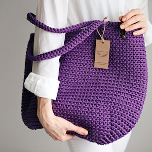 May include: A purple crocheted tote bag with a brown paper tag that reads "Thank you for purchasing our handmade crocheted tote bag".