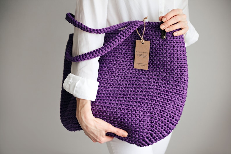 May include: A purple crocheted tote bag with a brown paper tag that reads "Thank you for purchasing our handmade crocheted tote bag".