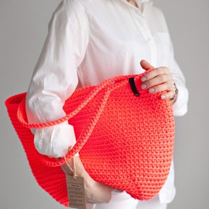 May include: A bright neon pink crocheted tote bag with black leather handles. The bag is large and roomy, perfect for carrying all your essentials.