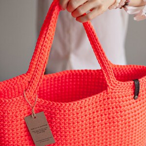 May include: A bright neon orange crocheted tote bag with a brown tag that says "Thank you for supporting the power of 100% handmade crochet bags".