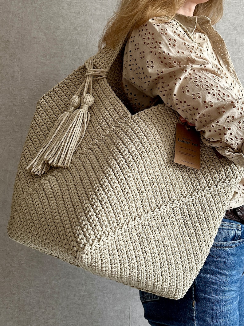 May include: A large, beige crocheted tote bag with a long tassel. The bag has a simple, textured design and is made with thick yarn.