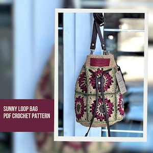 Può includere: Borsa all'uncinetto fatta a mano con un motivo floreale nei toni del bordeaux, verde e beige. La borsa presenta cinturini in pelle marrone e una chiusura con coulisse. Il testo "SUNNY LOOP BAG PDF CROCHET PATTERN" è visibile.