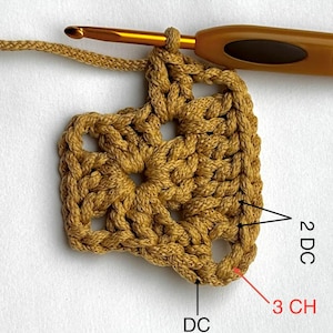 May include: Close-up of a crocheted granny square in a warm, golden-brown hue. The square is partially completed, with a crochet hook inserted. The image shows the stitches labeled as DC and CH.