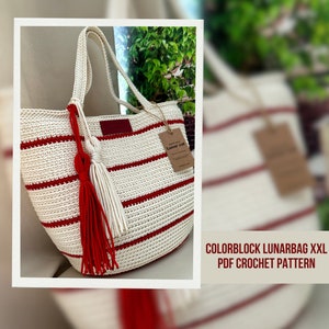 May include: A white and red striped crochet tote bag with a red tassel. The bag has a brown tag with the text "Lunar cot" on it. The image text reads "COLORBLOCK LUNARBAG XXL PDF CROCHET PATTERN".