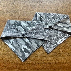 May include: Two reversible dog bandanas in a gray and white camouflage pattern and a gray and white checkered pattern. The bandanas have a snap closure and a white label that says "The Wagged Dog Company".