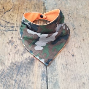 May include: A reversible bandana with a camouflage pattern on one side and a solid orange color on the other side. The bandana has a snap closure.