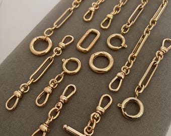 May include: A collection of gold-toned jewelry components including various chain segments with lobster claw clasps, spring ring clasps, a rectangular link, and a T-bar toggle closure. These metal findings feature polished surfaces and link designs.