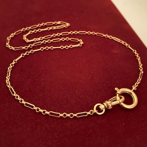 May include: A gold-toned chain necklace featuring a repeating pattern of elongated rectangular links connected by small circular links. The necklace includes a circular spring ring clasp attached to a swivel lobster claw clasp at one end.