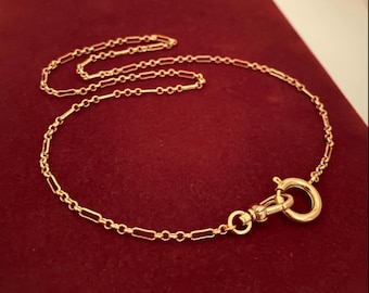 Può includere: Una collana a catena color oro caratterizzata da un motivo ripetitivo di maglie rettangolari allungate collegate da piccoli anelli circolari. La collana include una chiusura a molla circolare fissata a un moschettone girevole a un'estremità.