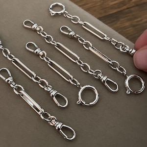 May include: Silver-toned metal chain extenders with various clasp styles. The extenders feature a combination of chain links, rectangular bars, and spring ring clasps. The image shows several extenders, showcasing their design and functionality.