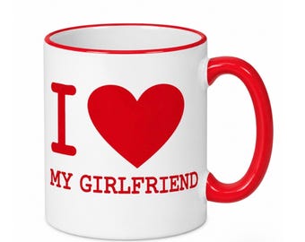 May include: A white ceramic mug with a red handle and red rim. The front of the mug features the red text I, a large red heart symbol, and the red text MY GIRLFRIEND printed in a bold, sans-serif font below the heart.