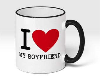 May include: A white ceramic mug featuring a black handle and a black rim. The front of the mug displays the text I, a large red heart symbol, and the text MY BOYFRIEND in black capital letters, arranged in a clear, centered graphic design.