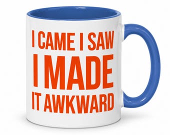 May include: A white ceramic mug with a blue interior and handle. The exterior features the orange text I CAME I SAW I MADE IT AWKWARD printed in a bold, sans-serif font. The mug has a cylindrical body and a curved handle on the right side.