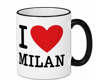 May include: A white ceramic mug with a black rim and a black handle. The front of the mug features the text I, a large red heart symbol, and the word MILAN printed in bold black capital letters below the heart.