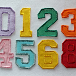 May include: A collection of colorful, embroidered number patches, including zero through eight. Each number is a different color, with a contrasting border. The patches are likely for crafts or personalization.
