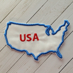 May include: A white fabric patch in the shape of the United States of America with a blue outline and the word "USA" embroidered in red.