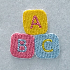 May include: An embroidered patch featuring three square blocks arranged in a pyramid shape. The top block is yellow with a pink letter A. The bottom left block is pink with a light blue letter B, and the bottom right block is light blue with a yellow letter C.